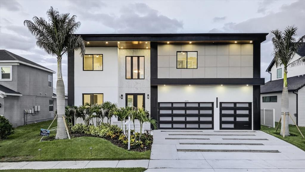 A modern two-story house with a flat roof, dark trim, and a three-car garage at dusk — 3420 CHANNELSIDE COURT, SAFETY HARBOR, FL
