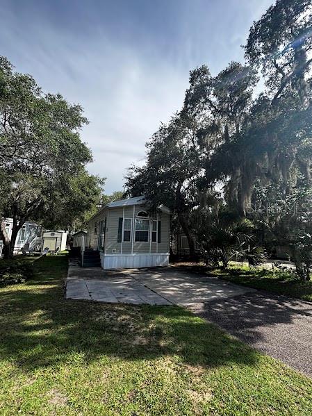 A light-colored mobile home sits on a paved lot surrounded by large, moss-draped oak trees — 25296 141ST STREET NE UNIT 380, FORT MC COY, FL