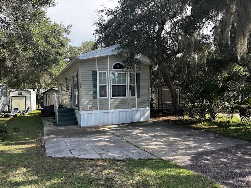 A light-colored manufactured home with green shutters sits on a concrete driveway under trees — 25296 141ST STREET NE UNIT 380, FORT MC COY, FL