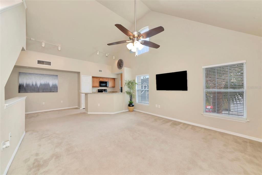 A living room with vaulted ceilings, beige carpet, a ceiling fan, and an open kitchen — 5560 ROSEHILL ROAD UNIT 201, SARASOTA, FL