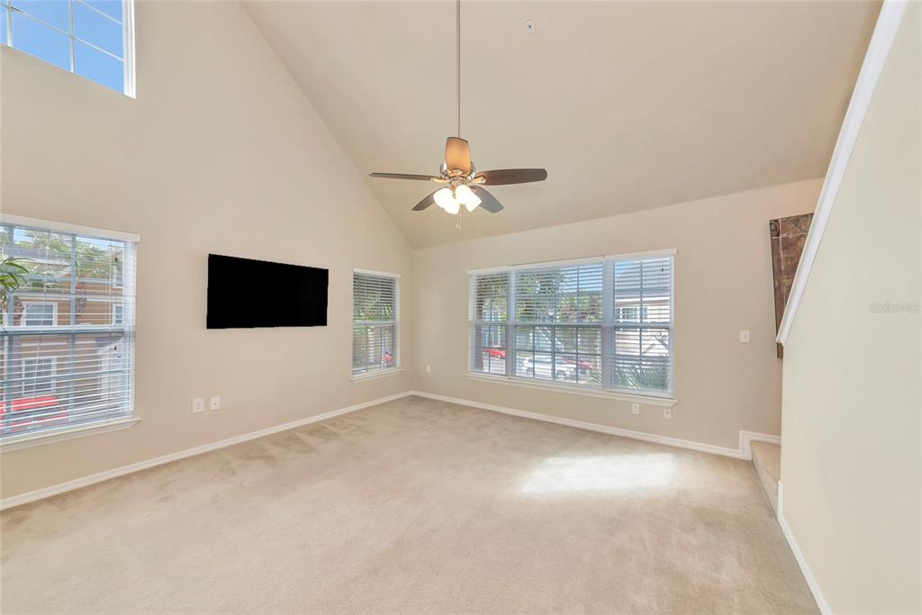 A living room with beige carpet, vaulted ceilings, a ceiling fan, and large windows — 5560 ROSEHILL ROAD UNIT 201, SARASOTA, FL