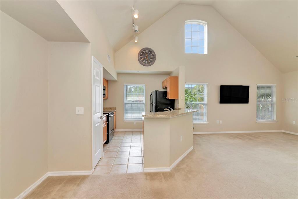 A kitchen with tile flooring and a breakfast bar opens into a carpeted living area — 5560 ROSEHILL ROAD UNIT 201, SARASOTA, FL