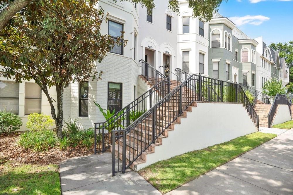 A multi-story townhouse exterior features white brick walls, black metal railings, and concrete stairs — 560 COPLEY LANE, ORLANDO, FL