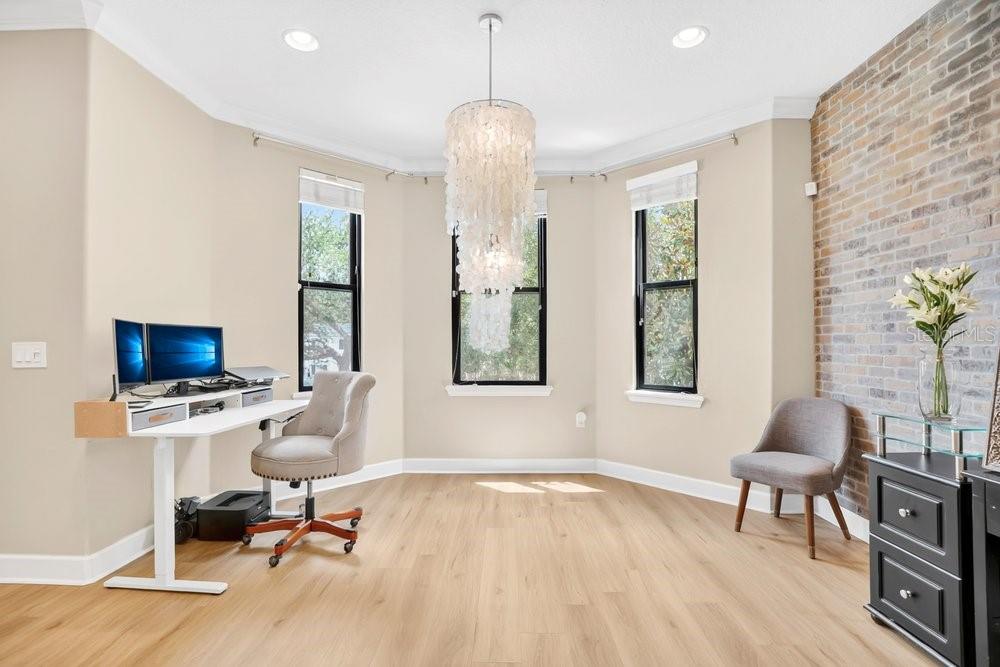 A home office features light wood flooring, a white desk, a chandelier, and a brick wall — 560 COPLEY LANE, ORLANDO, FL