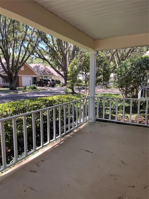 A covered concrete porch features white railings overlooking a residential street with trees and houses — 8591 SW 93RD PLACE UNIT E, OCALA, FL