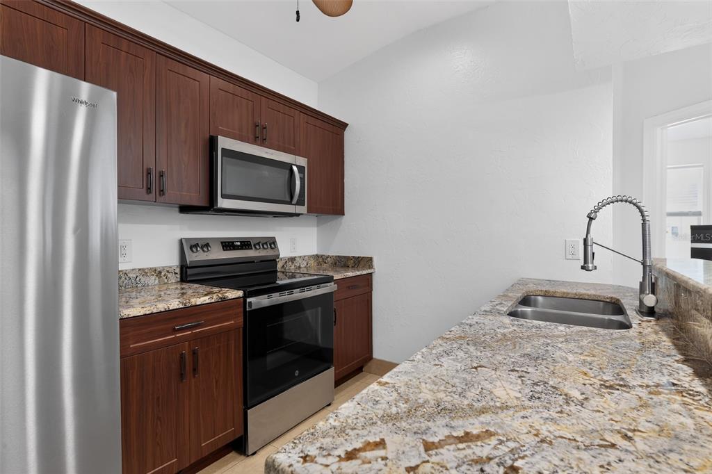 A kitchen features dark wood cabinets, granite countertops, and stainless steel appliances — 1816 RITA STREET, SARASOTA, FL