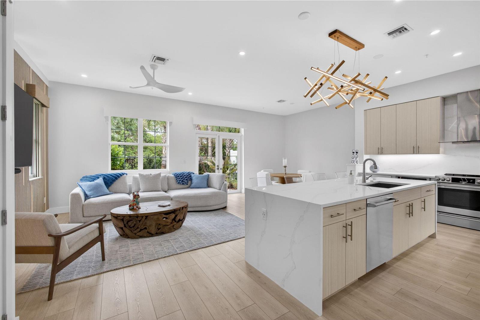 An open-concept living room and kitchen featuring light wood floors, a white island, and furniture — 130 Water Pointe Place # 7, Jupiter FL 33477, JUPITER, FL