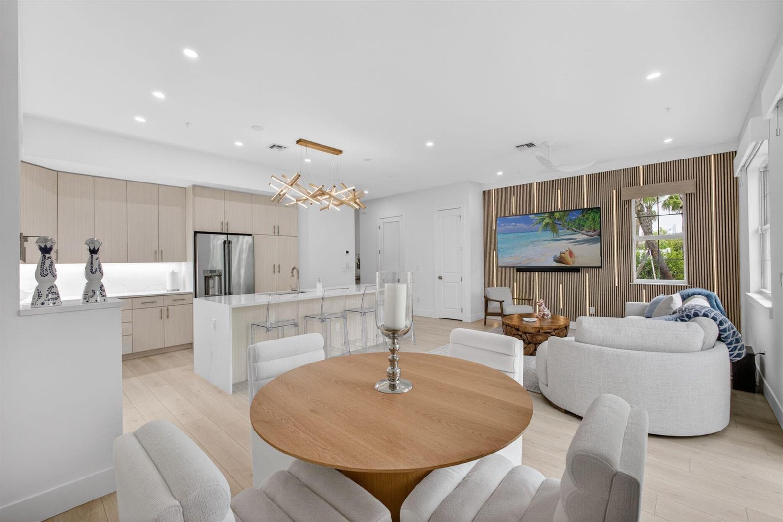 An open-concept kitchen and living area features light wood cabinetry, a round dining table, and slatted wall accents — 130 Water Pointe Place # 7, Jupiter FL 33477, JUPITER, FL