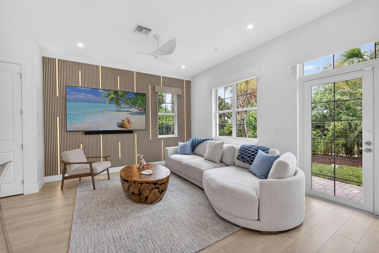 A living room features a slatted wood accent wall, a curved sofa, and a round table — 130 Water Pointe Place # 7, Jupiter FL 33477, JUPITER, FL