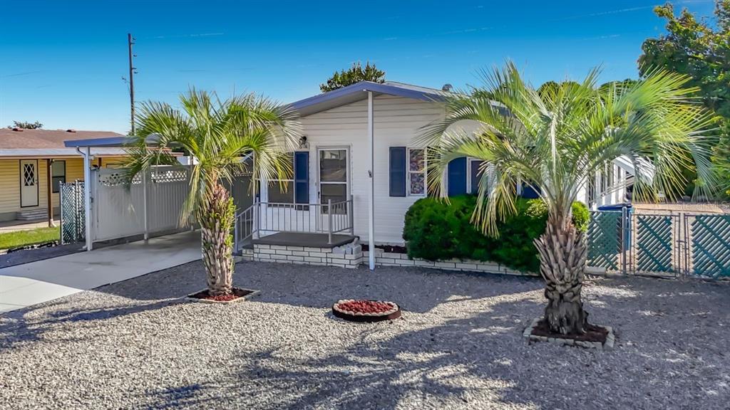 A single-story mobile home features white siding, a gravel yard, and two palm trees — 15116 BROOKRIDGE BOULEVARD, BROOKSVILLE, FL