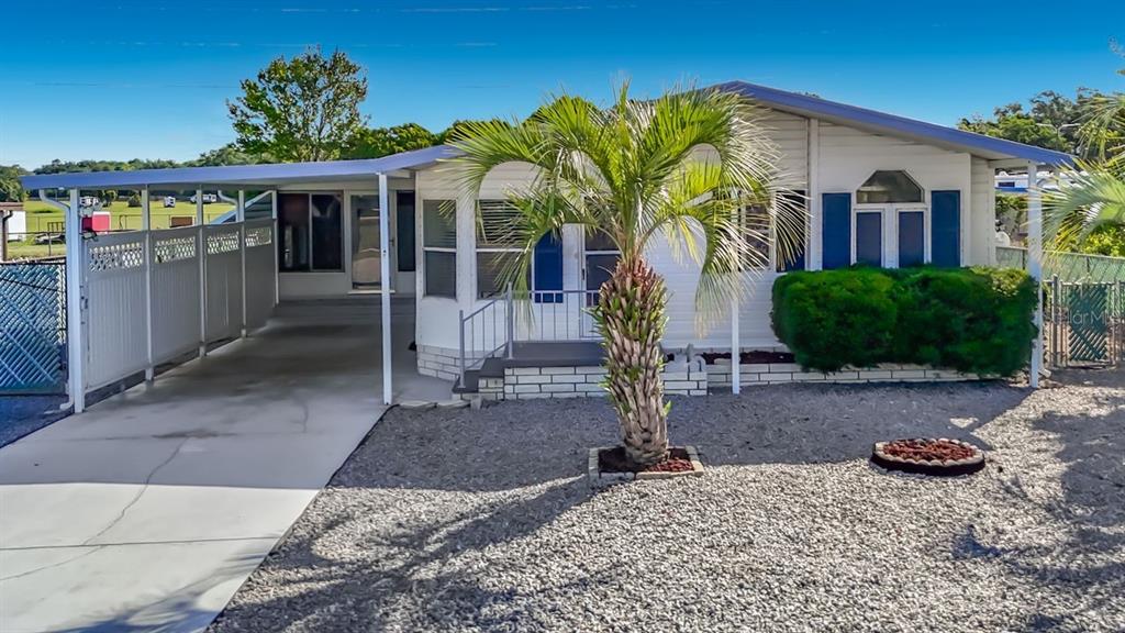 A single-story manufactured home features a carport, a palm tree, and a gravel front yard — 15116 BROOKRIDGE BOULEVARD, BROOKSVILLE, FL