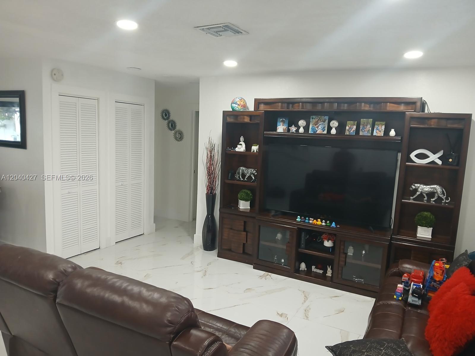 A living room features a large wooden entertainment center, brown leather sofas, and white tile flooring — 235 SW 18th Ave, Homestead FL 33030, HOMESTEAD, FL