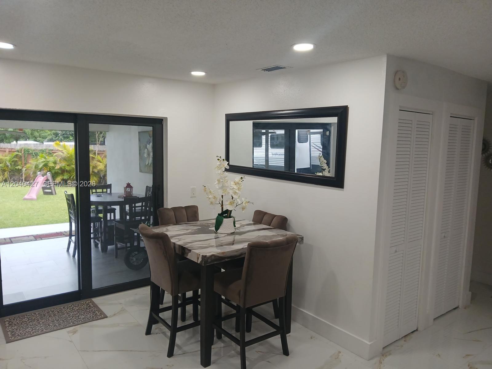 A dining area features a marble-topped table, brown chairs, a wall mirror, and sliding glass doors — 235 SW 18th Ave, Homestead FL 33030, HOMESTEAD, FL