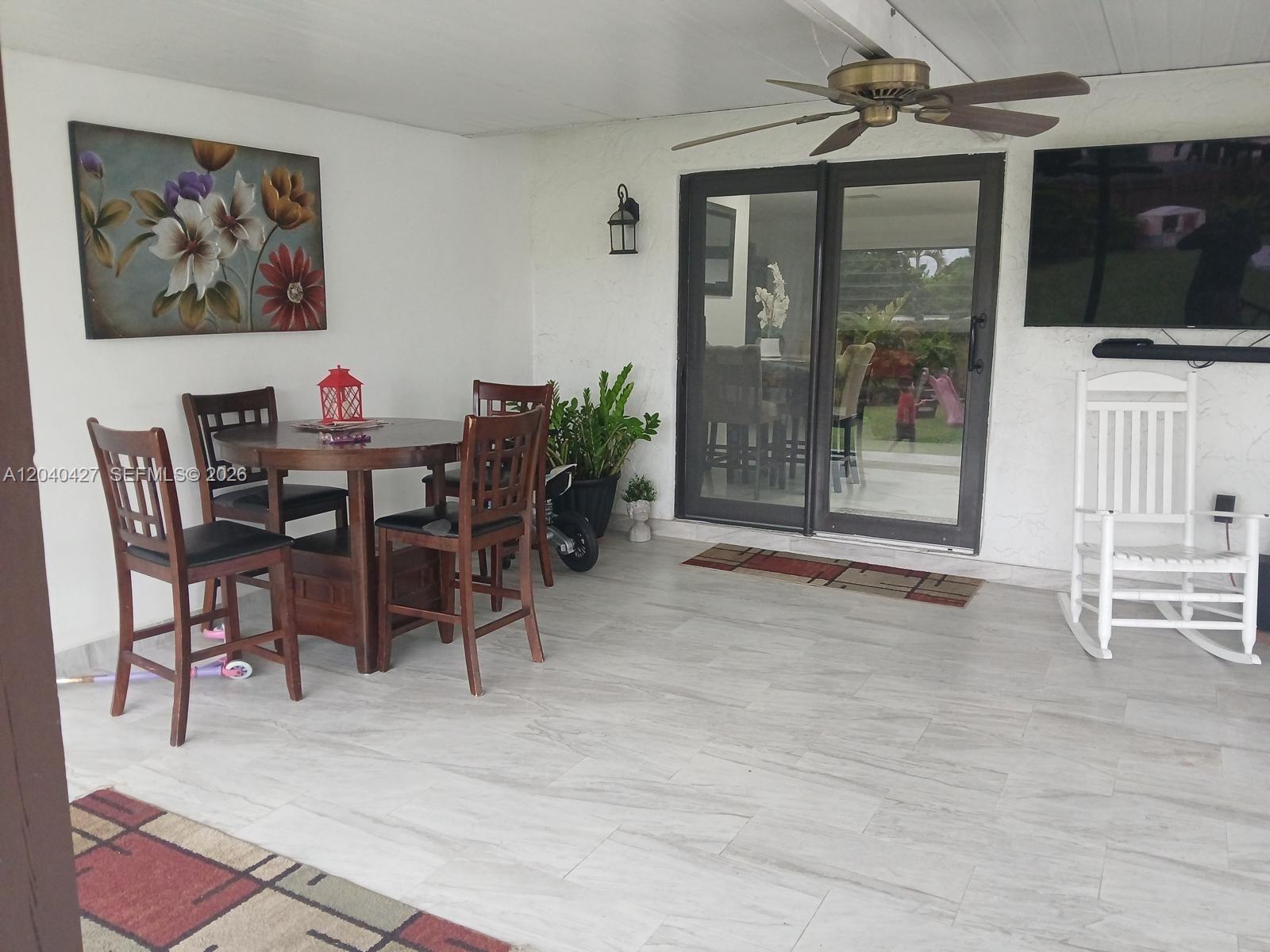 A covered patio features a dining set, a white rocking chair, and a ceiling fan — 235 SW 18th Ave, Homestead FL 33030, HOMESTEAD, FL