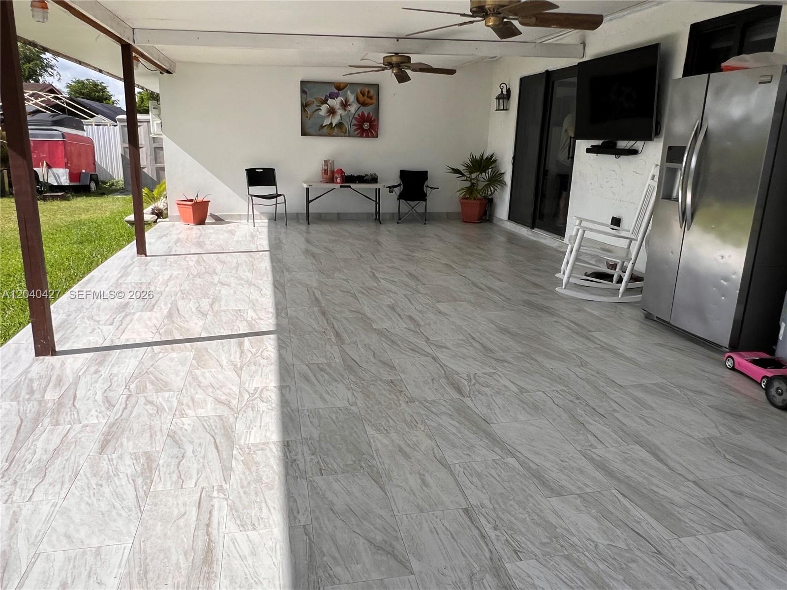 A covered outdoor patio features light-colored tile flooring, two ceiling fans, and a stainless refrigerator — 235 SW 18th Ave, Homestead FL 33030, HOMESTEAD, FL