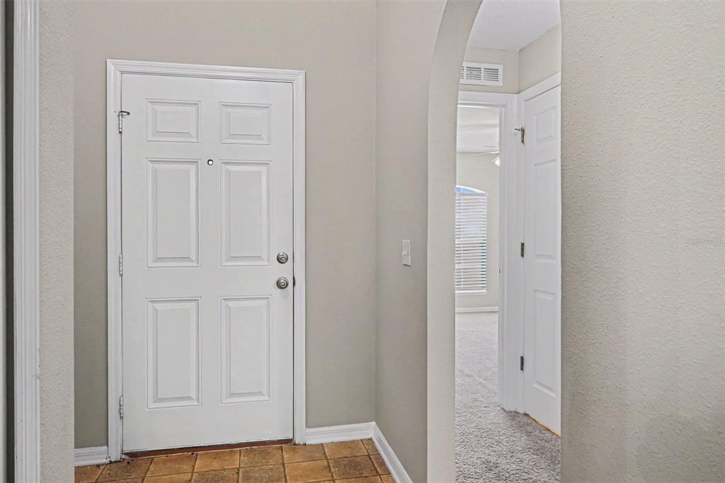 An entryway features a white front door, tiled flooring, and an arched doorway leading inside — 1761 EAGLE PINES CIRCLE, EAGLE LAKE, FL