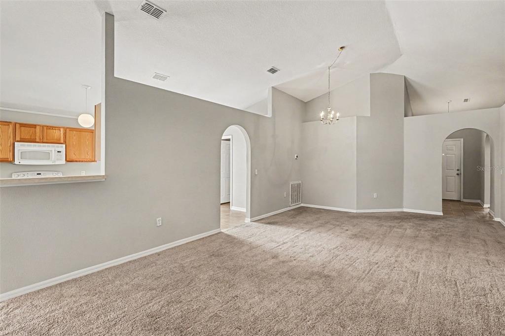 A living room with beige carpet, gray walls, vaulted ceilings, and two arched doorways — 1761 EAGLE PINES CIRCLE, EAGLE LAKE, FL