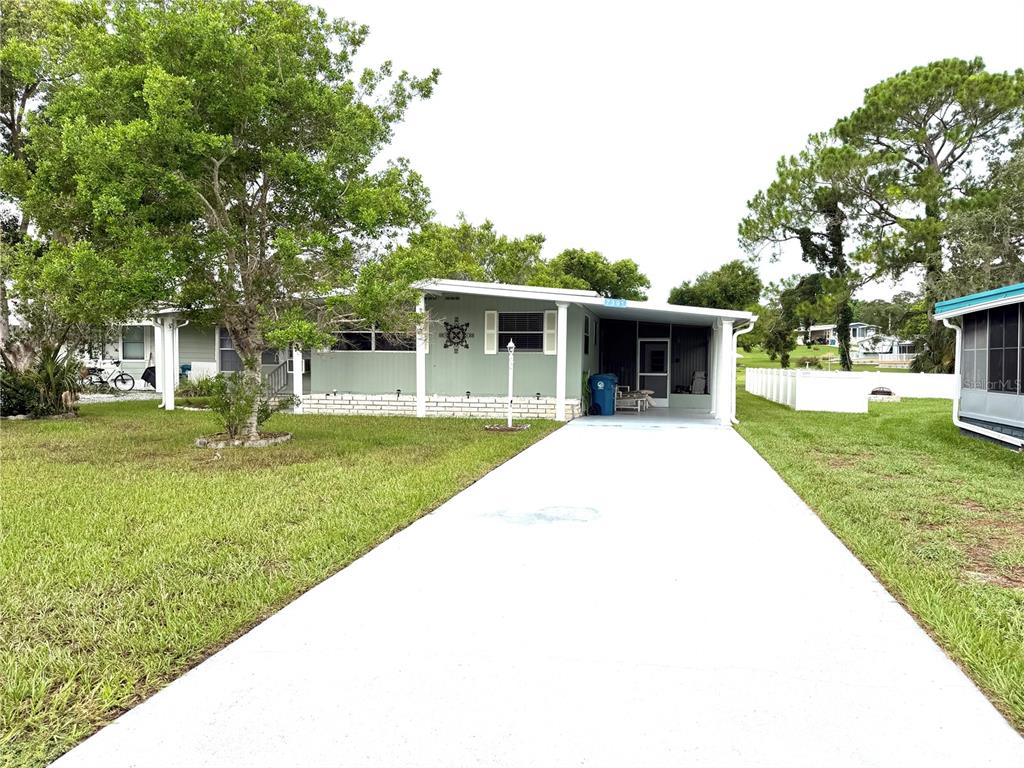 A single-story mobile home with a light green exterior, a white driveway, and a carport — 7391 HARLOW STREET, BROOKSVILLE, FL