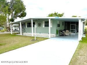 A light green mobile home features a white carport and a covered front porch — 7391 HARLOW STREET, BROOKSVILLE, FL