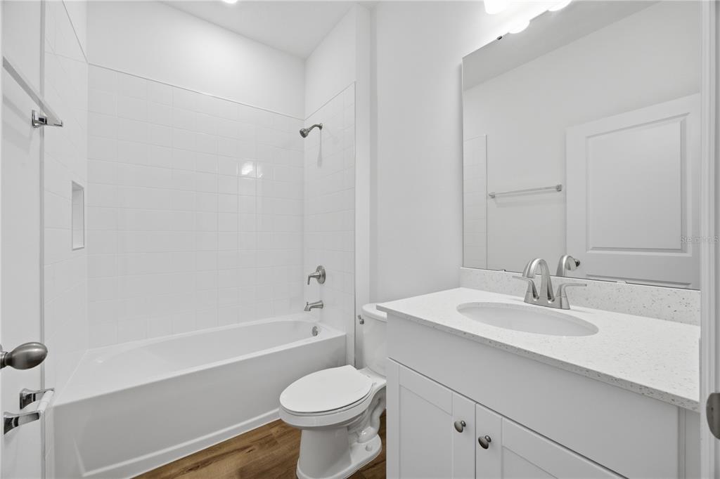 A bathroom features a white vanity, a toilet, and a bathtub with white tile walls — 5727 HIAWASSEE ROAD, OKAHUMPKA, FL