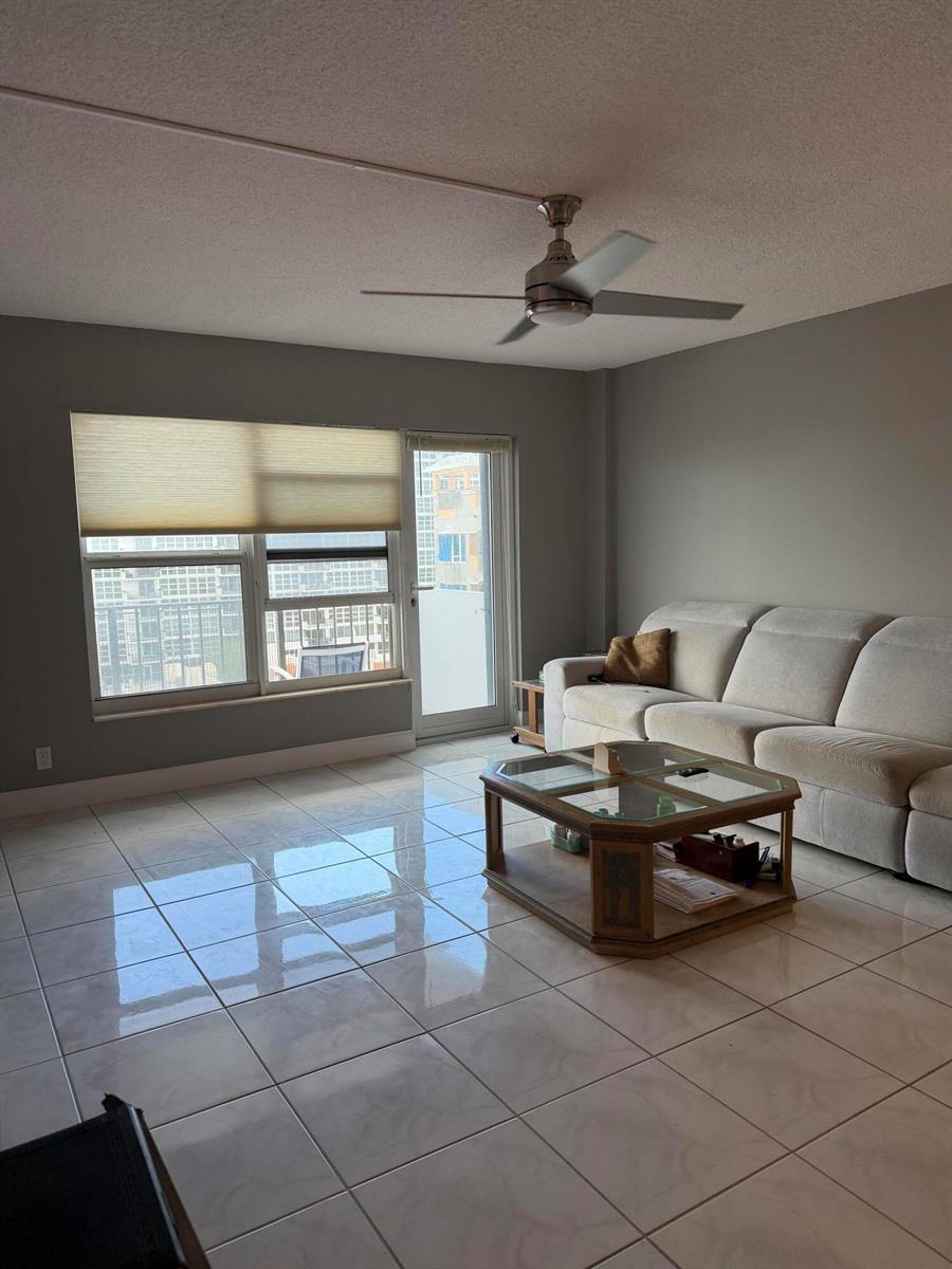 A living room features light-colored tile flooring, a ceiling fan, and a glass-topped coffee table — 405 N Ocean Boulevard # 809, Pompano Beach FL 33062, POMPANO BEACH, FL