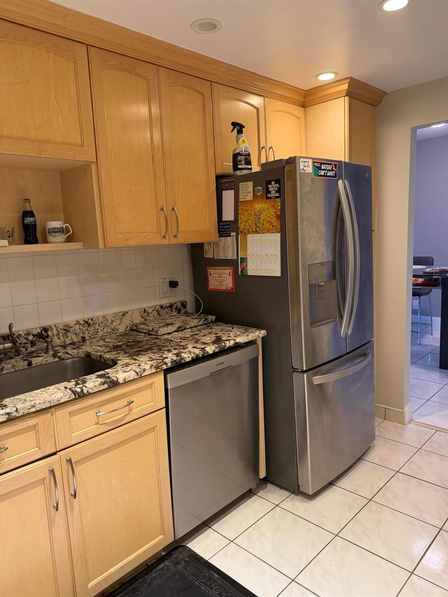 A kitchen features light wood cabinets, granite countertops, a stainless steel dishwasher, and a refrigerator — 405 N Ocean Boulevard # 809, Pompano Beach FL 33062, POMPANO BEACH, FL