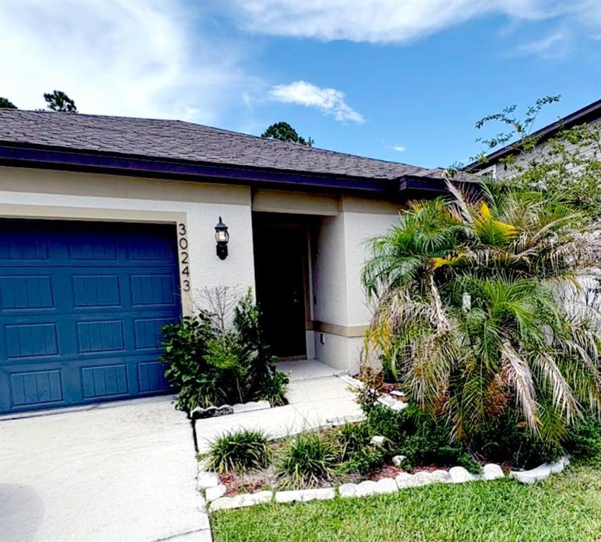 A single-story house exterior features a blue garage door, a front entrance, and landscaping — 30243 MARQUETTE AVENUE, WESLEY CHAPEL, FL