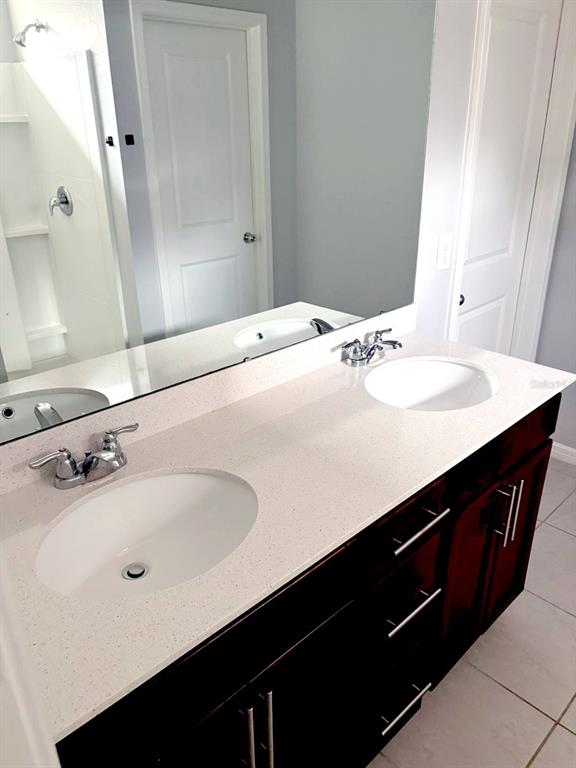 A bathroom vanity with a white speckled countertop, dual sinks, and dark wood cabinets — 30243 MARQUETTE AVENUE, WESLEY CHAPEL, FL