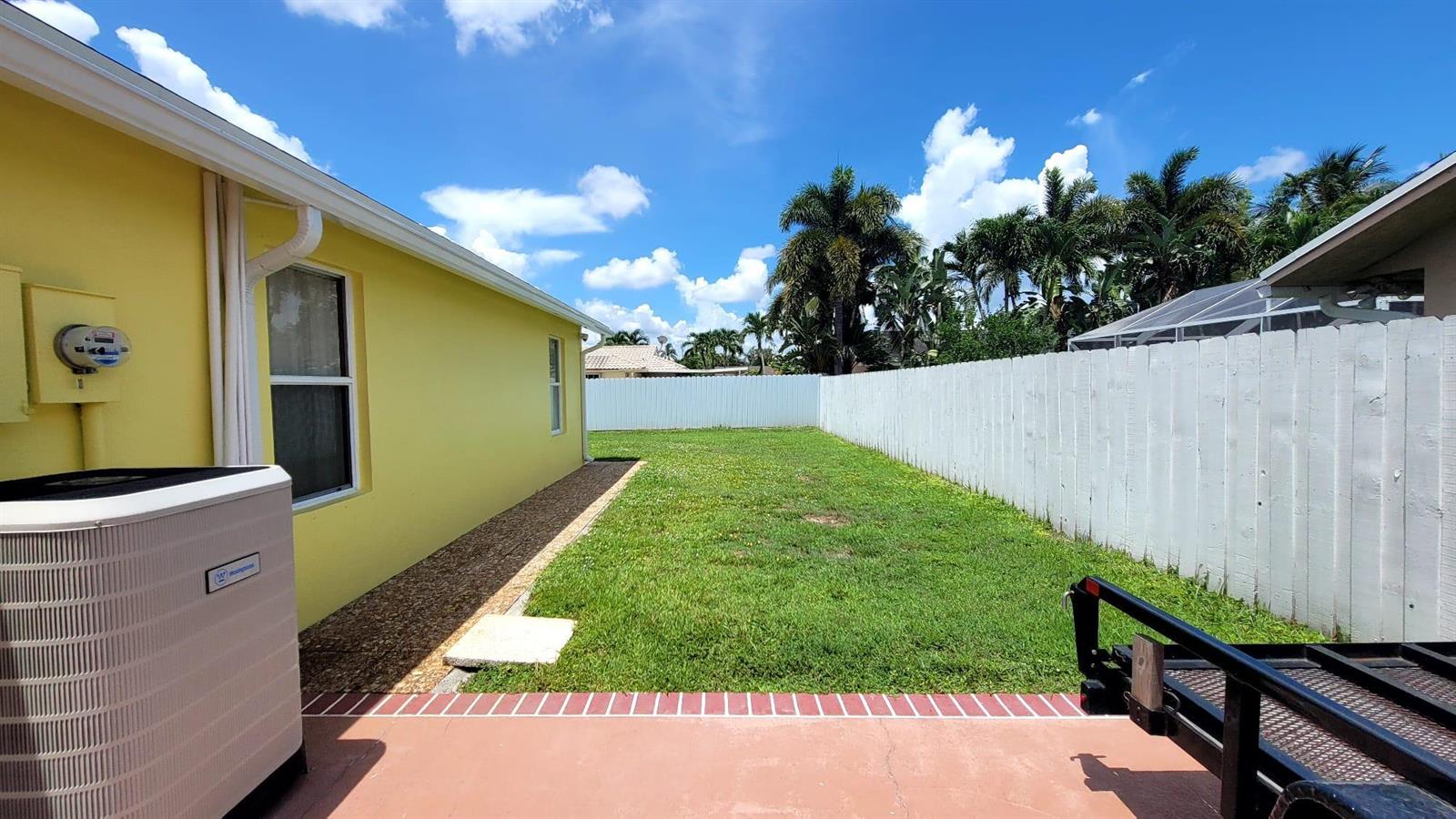 A yellow house exterior with an air conditioning unit, a grassy yard, and a white fence — WELLINGTON, FL