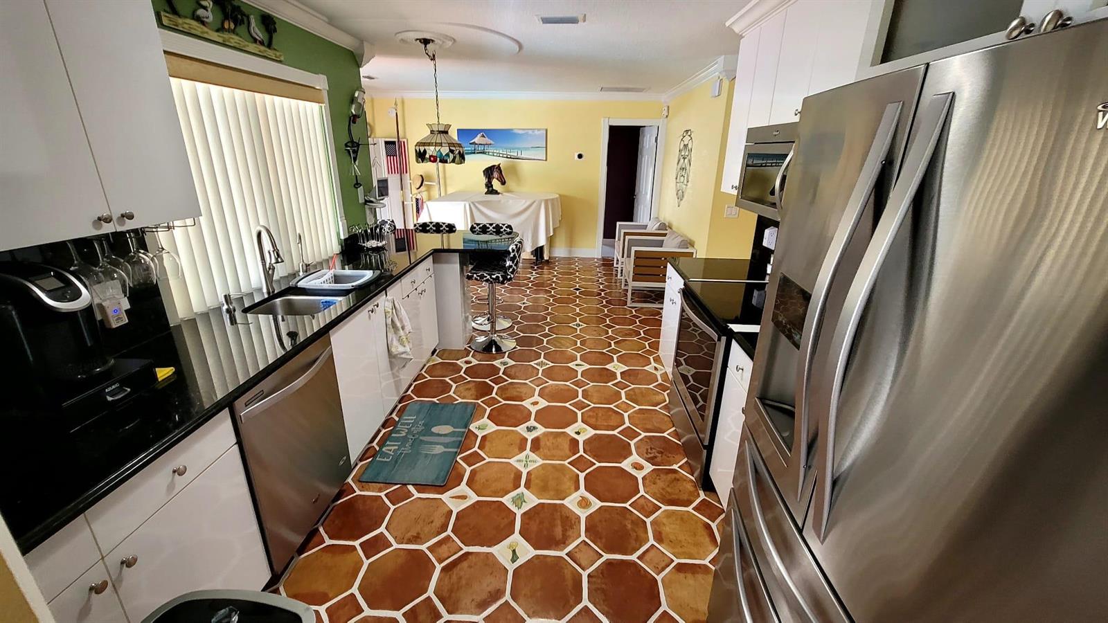 A kitchen features stainless steel appliances, white cabinets, black countertops, and hexagonal floor tiles — WELLINGTON, FL