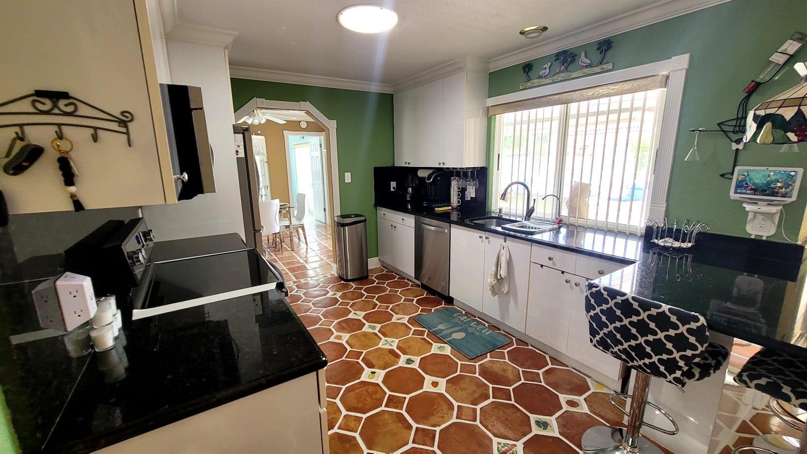 A kitchen features white cabinets, black countertops, green walls, and hexagonal terracotta-style floor tiles — WELLINGTON, FL