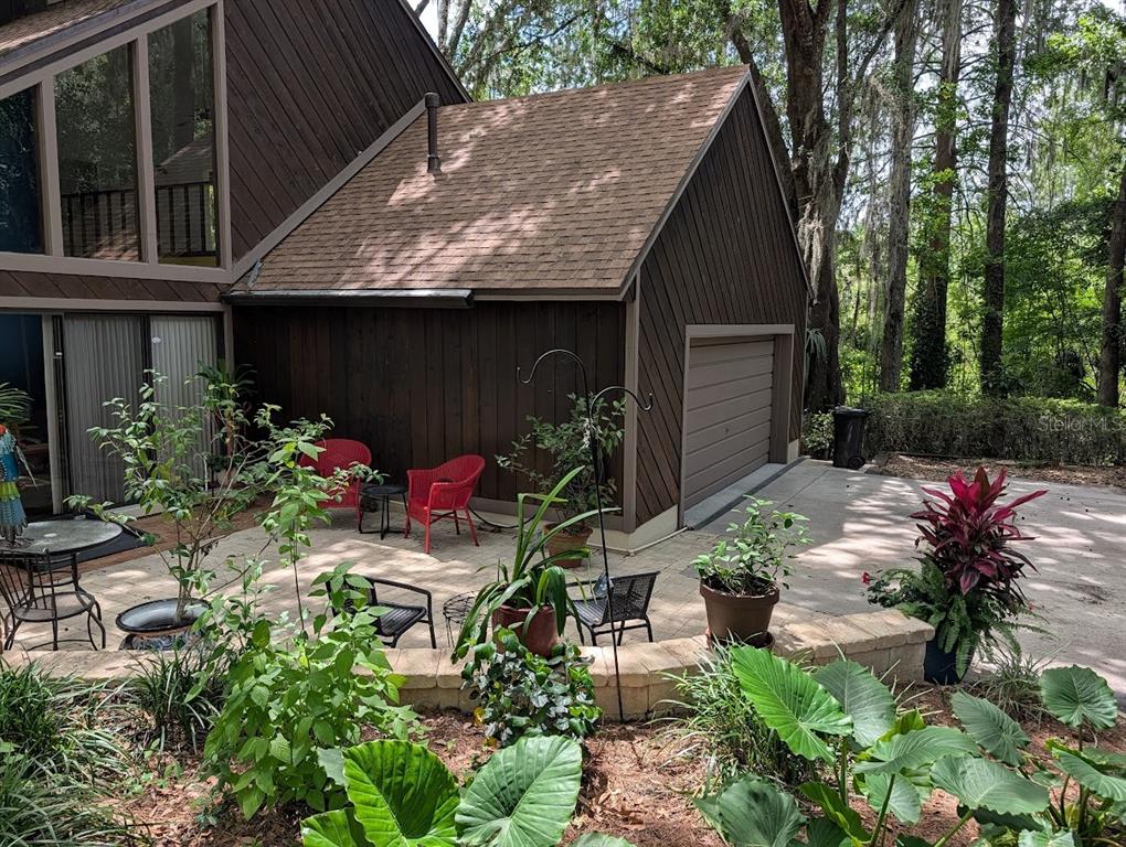 A brown house with a garage and a patio featuring red chairs and potted plants — 5902 SW 36TH WAY, GAINESVILLE, FL