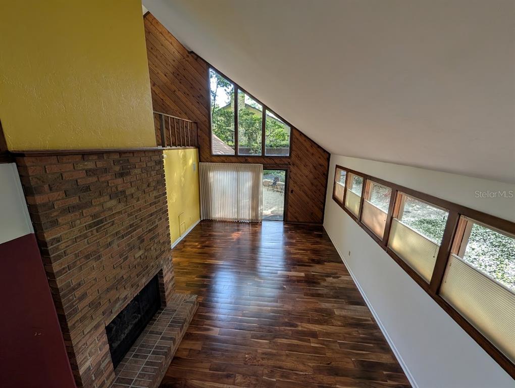 A living room features a brick fireplace, wood-paneled walls, hardwood floors, and large angled windows — 5902 SW 36TH WAY, GAINESVILLE, FL