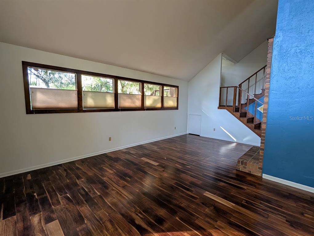 A living room with dark hardwood floors, a large window bank, and a wooden staircase — 5902 SW 36TH WAY, GAINESVILLE, FL