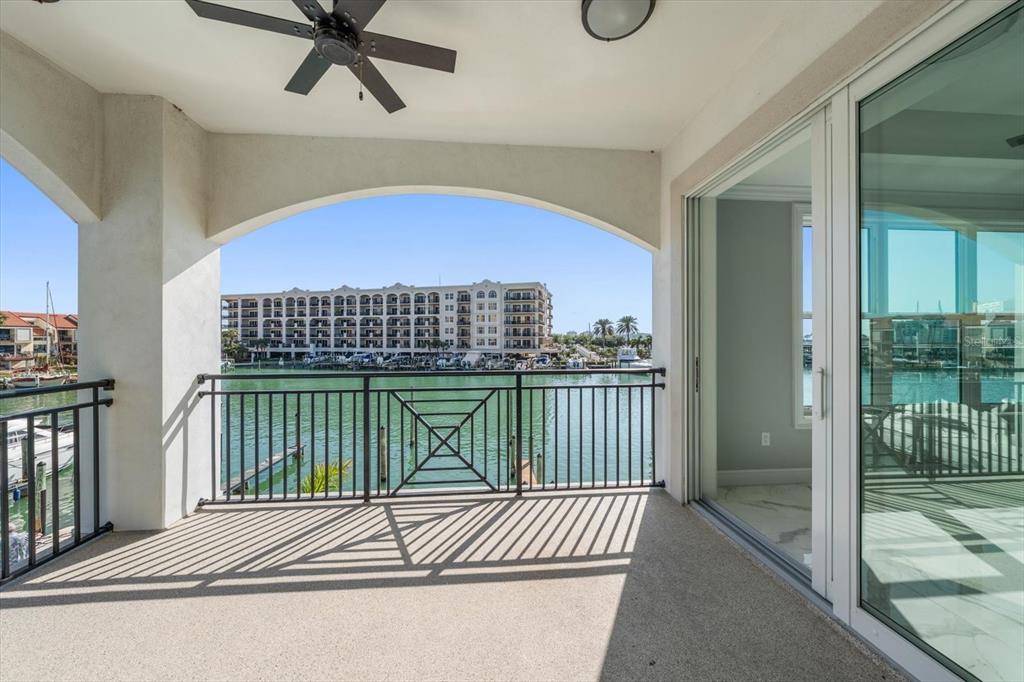 A covered balcony with a ceiling fan overlooks a canal and a large apartment building — 211 DOLPHIN POINT UNIT 201, CLEARWATER, FL