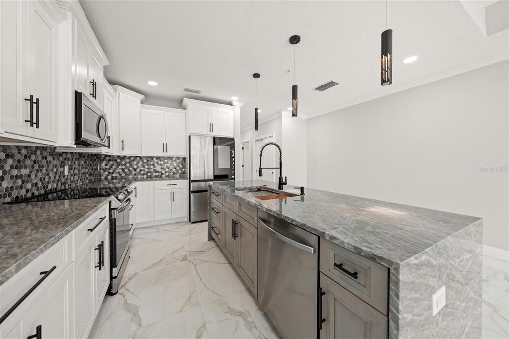 A modern kitchen features white upper cabinets, gray lower cabinets, and a stone-topped island — 211 DOLPHIN POINT UNIT 201, CLEARWATER, FL