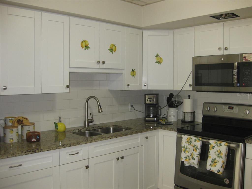 A kitchen features white cabinets with lemon decals, granite countertops, and stainless steel appliances — 5860 43RD TERRACE N UNIT 1518, KENNETH CITY, FL