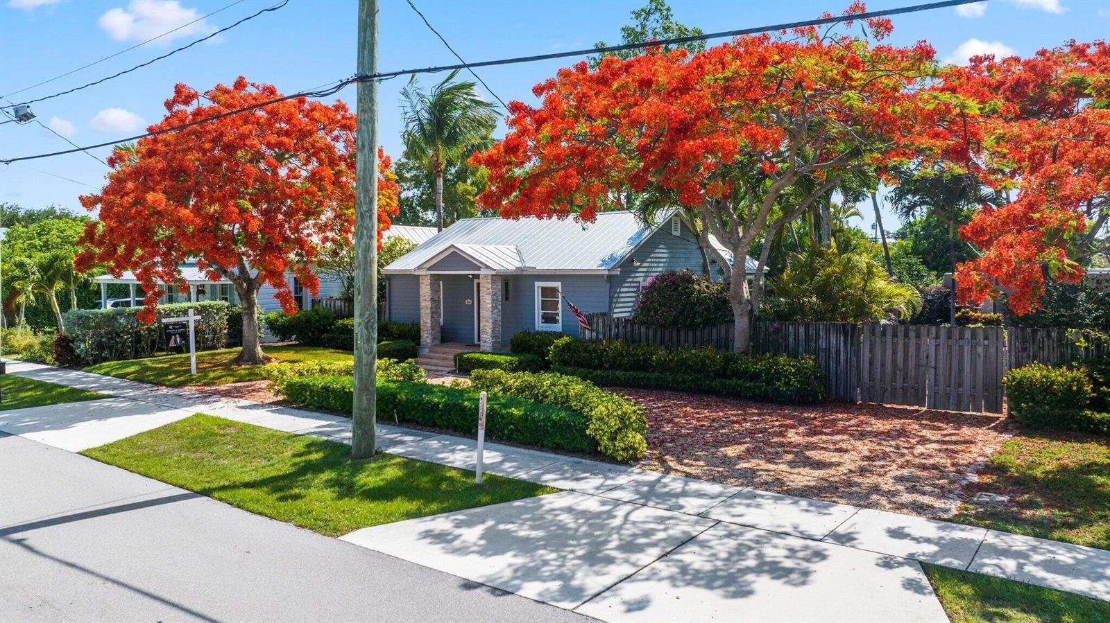 A gray house with a metal roof sits behind a wooden fence and flowering trees — 304 SE 4th Avenue, Delray Beach FL 33483, DELRAY BEACH, FL