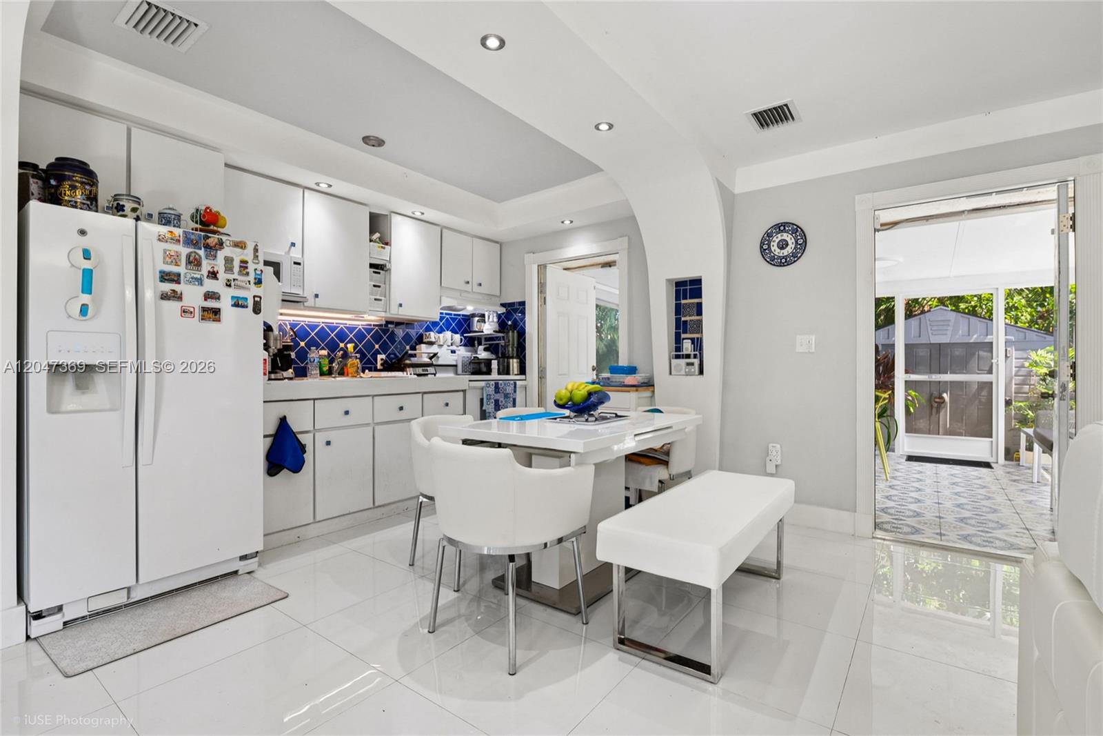A kitchen features white cabinetry, blue tile backsplashes, a dining table, and a patio door — 3750 Percival Ave, Miami FL 33133, MIAMI, FL
