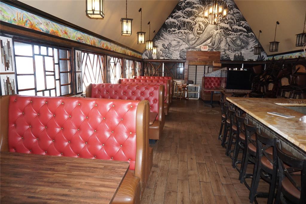 A restaurant interior features red tufted booths, wooden tables, a bar, and a mural wall — 5800 34TH STREET N, ST PETERSBURG, FL