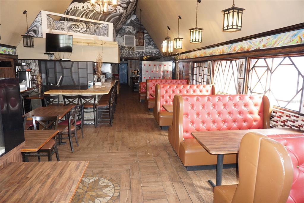A restaurant interior features red tufted booths, wooden tables, bar seating, and decorative lighting — 5800 34TH STREET N, ST PETERSBURG, FL
