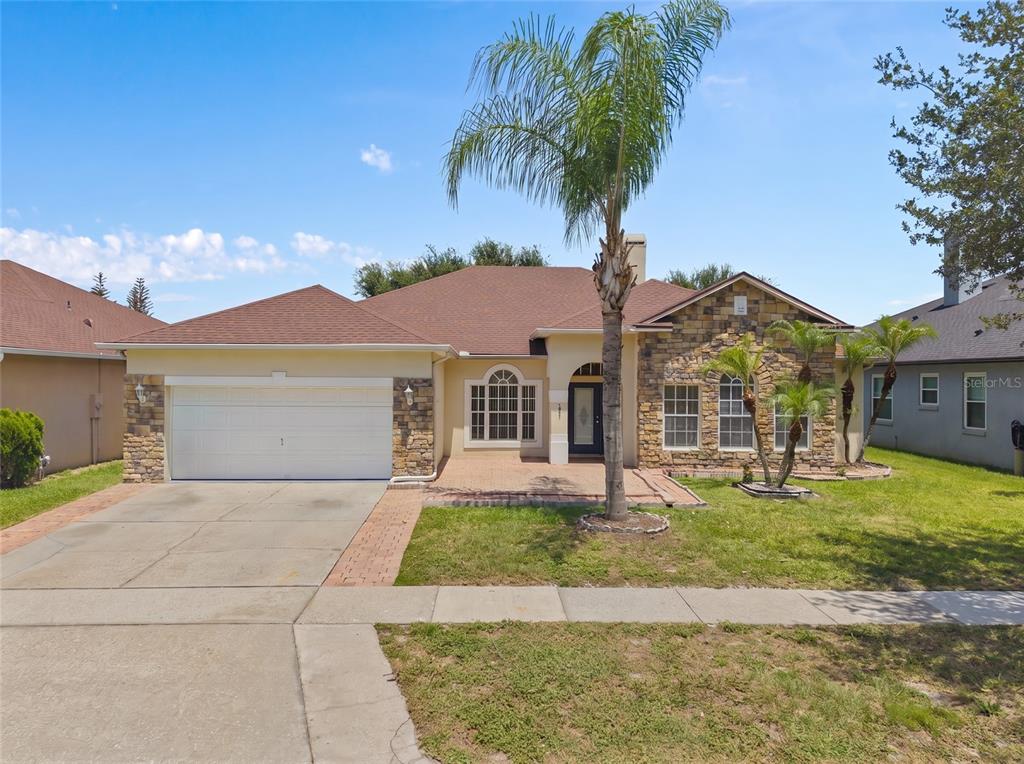 A single-story house with a stone facade, a palm tree, and a two-car garage — 13821 AMBERLEIGH ROAD, ORLANDO, FL