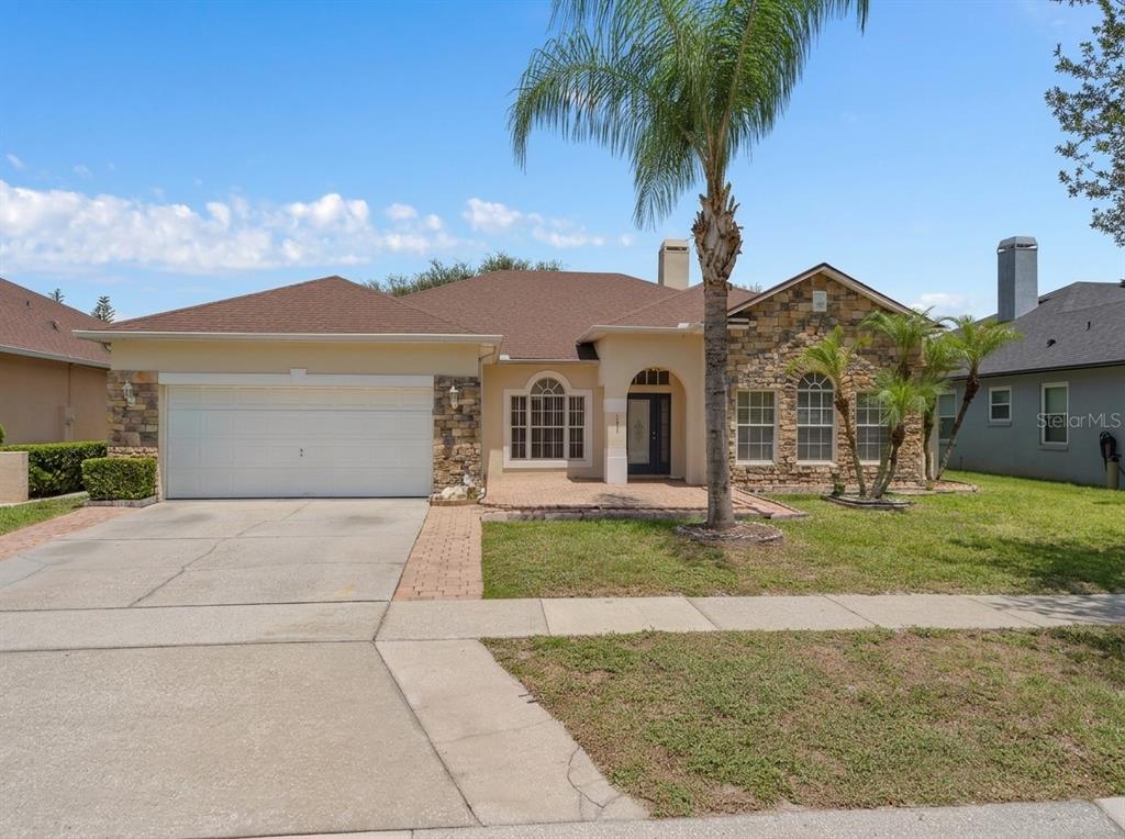A single-story house with a stone facade, a two-car garage, and a palm tree — 13821 AMBERLEIGH ROAD, ORLANDO, FL