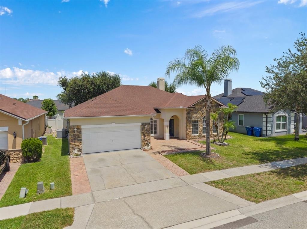 A single-story suburban house with a stone facade, brown roof, and a palm tree — 13821 AMBERLEIGH ROAD, ORLANDO, FL