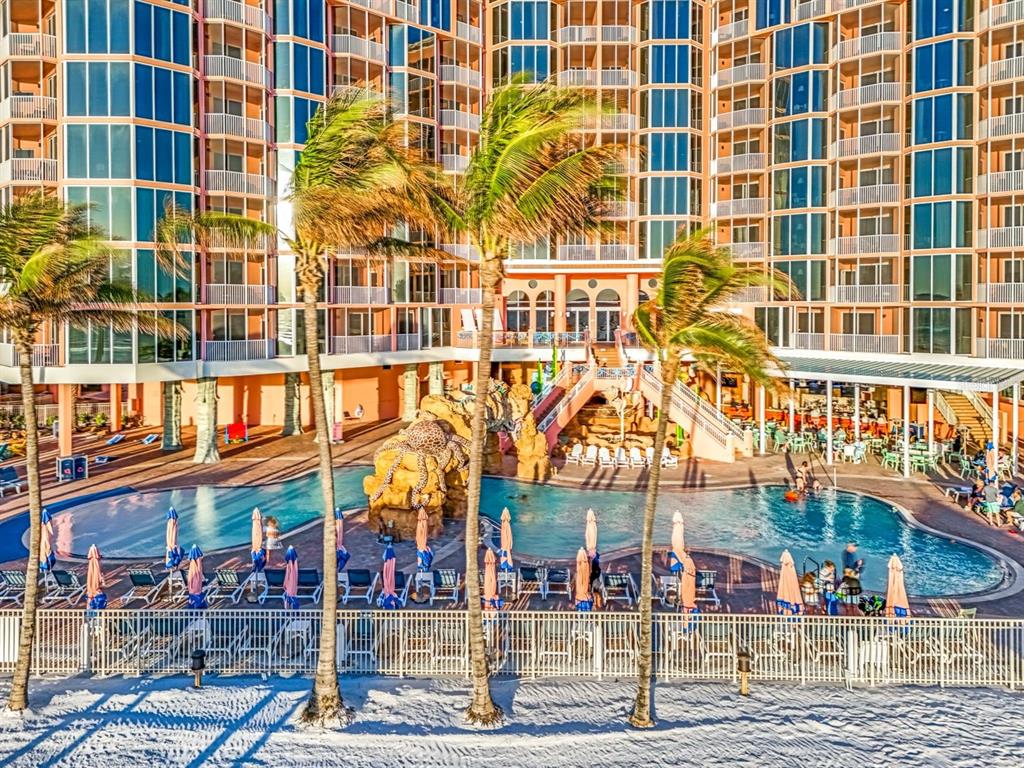An exterior view of a multi-story resort building with a swimming pool and palm trees — 200 ESTERO BOULEVARD UNIT 207, FORT MYERS BEACH, FL