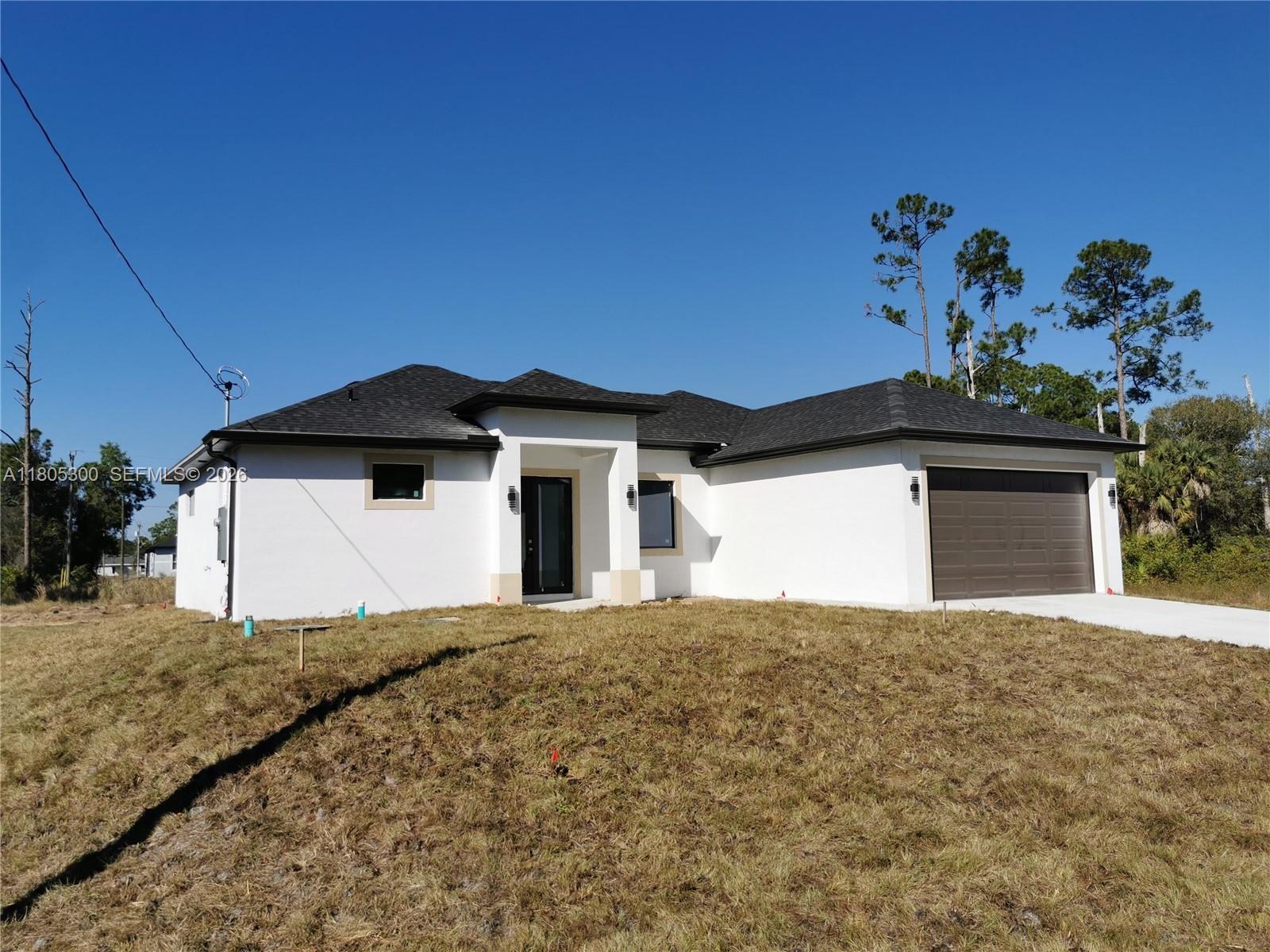 A newly constructed single-story house features white stucco walls, a dark roof, and a garage — 326 Nathan Ave, Lehigh Acres FL 33974, LEHIGH ACRES, FL