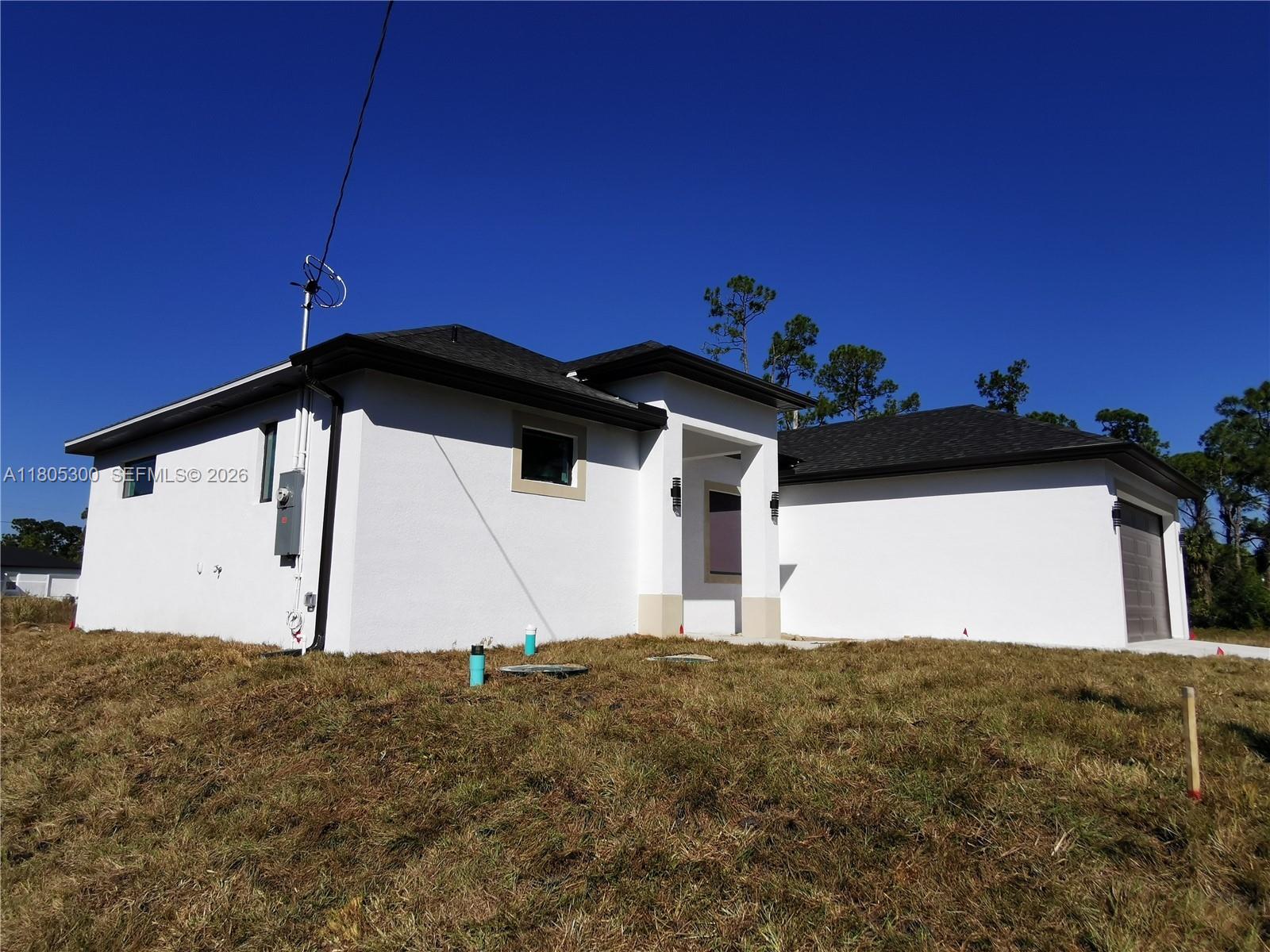 A white, single-story house with a dark roof stands on a grassy lot — 326 Nathan Ave, Lehigh Acres FL 33974, LEHIGH ACRES, FL