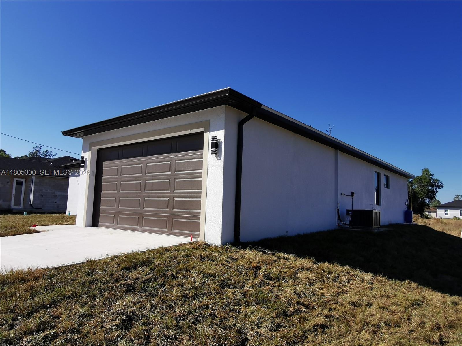 A white stucco house features a brown garage door and a concrete driveway — 326 Nathan Ave, Lehigh Acres FL 33974, LEHIGH ACRES, FL
