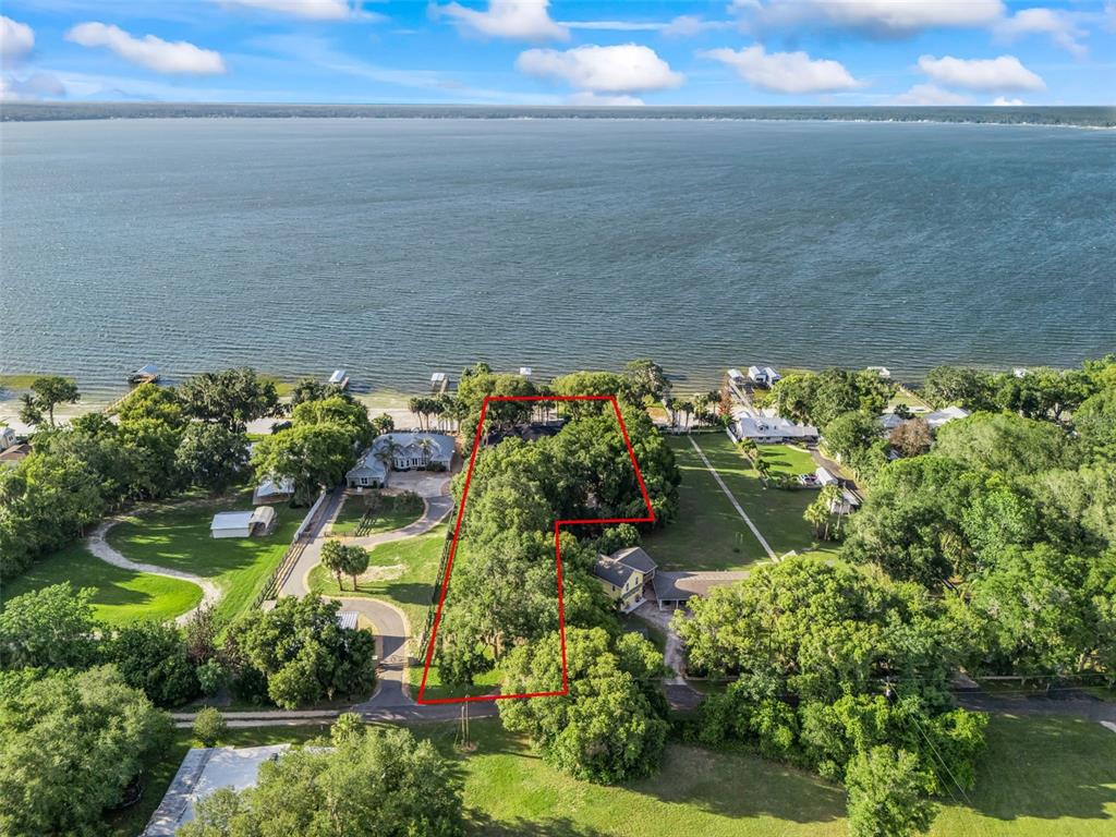 An aerial view shows a wooded waterfront lot outlined in red along a large lake — 13061 SE 158TH LANE, WEIRSDALE, FL