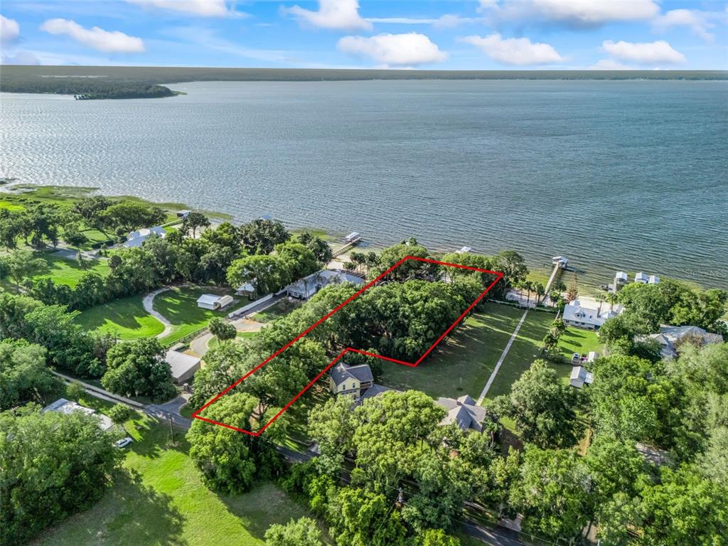 An aerial view shows a waterfront property lot outlined in red near a large lake — 13061 SE 158TH LANE, WEIRSDALE, FL